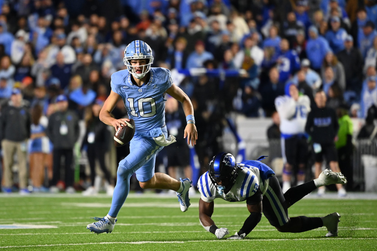 Drake Maye runs with the ball in one hand as he escapes a defender who tries to tackle him